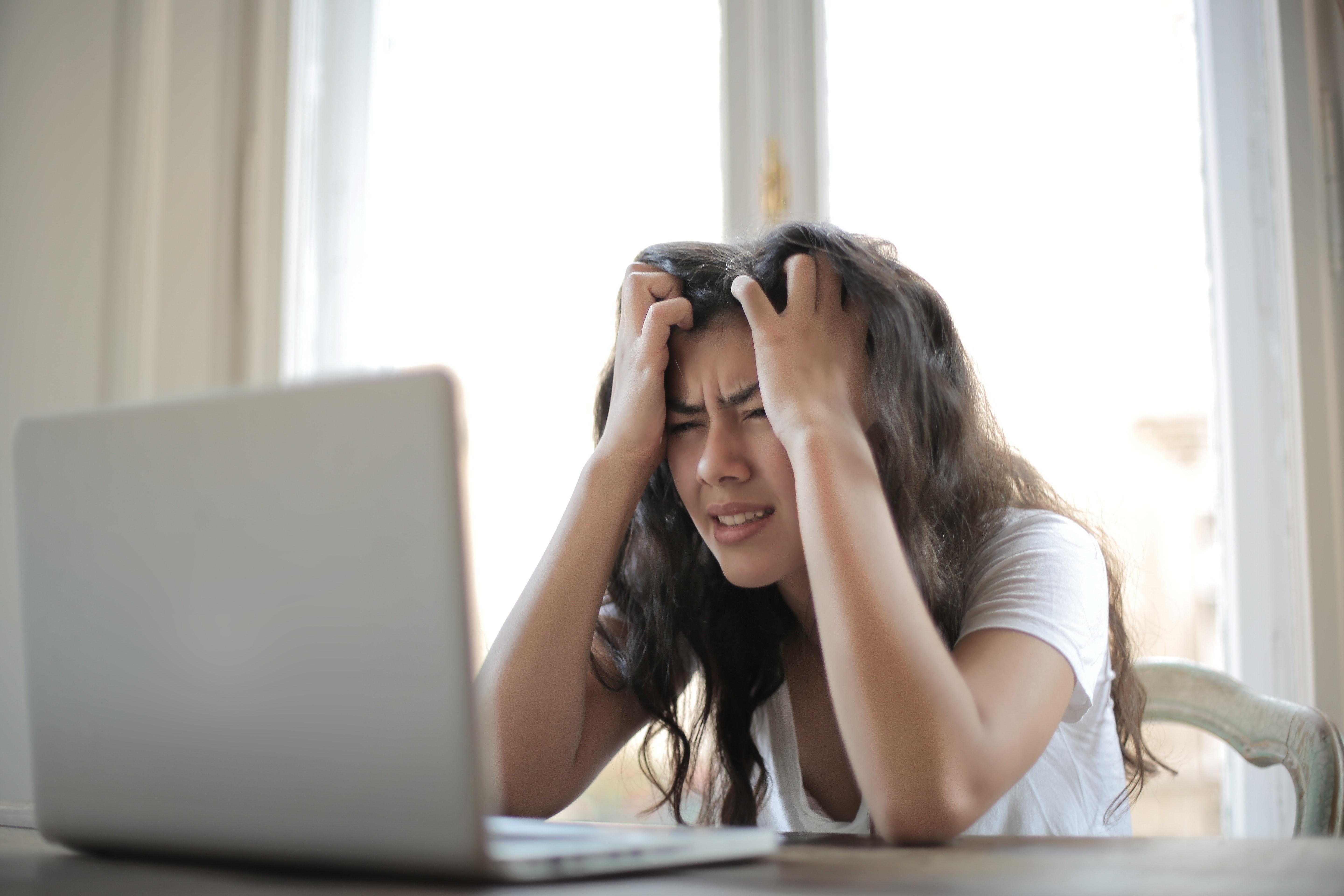 Girl in front of laptop holding her head in her hands