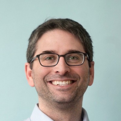 Gil Cohen- Man with dark hair and eyes with glasses and light blue dress shirt, smiling